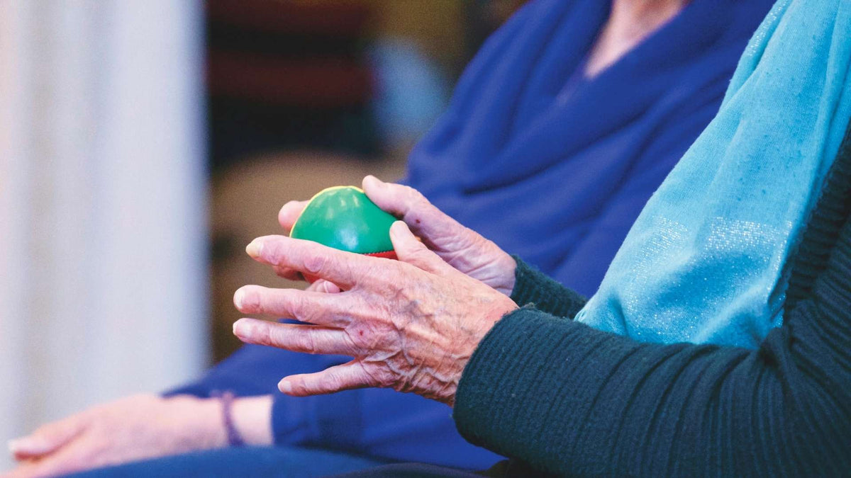 Close-up of a seated person holding a green exercise ball between their hands.
