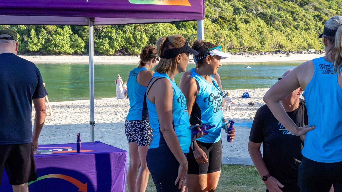 Running club members beside a purple fisiocrem stand by the water.