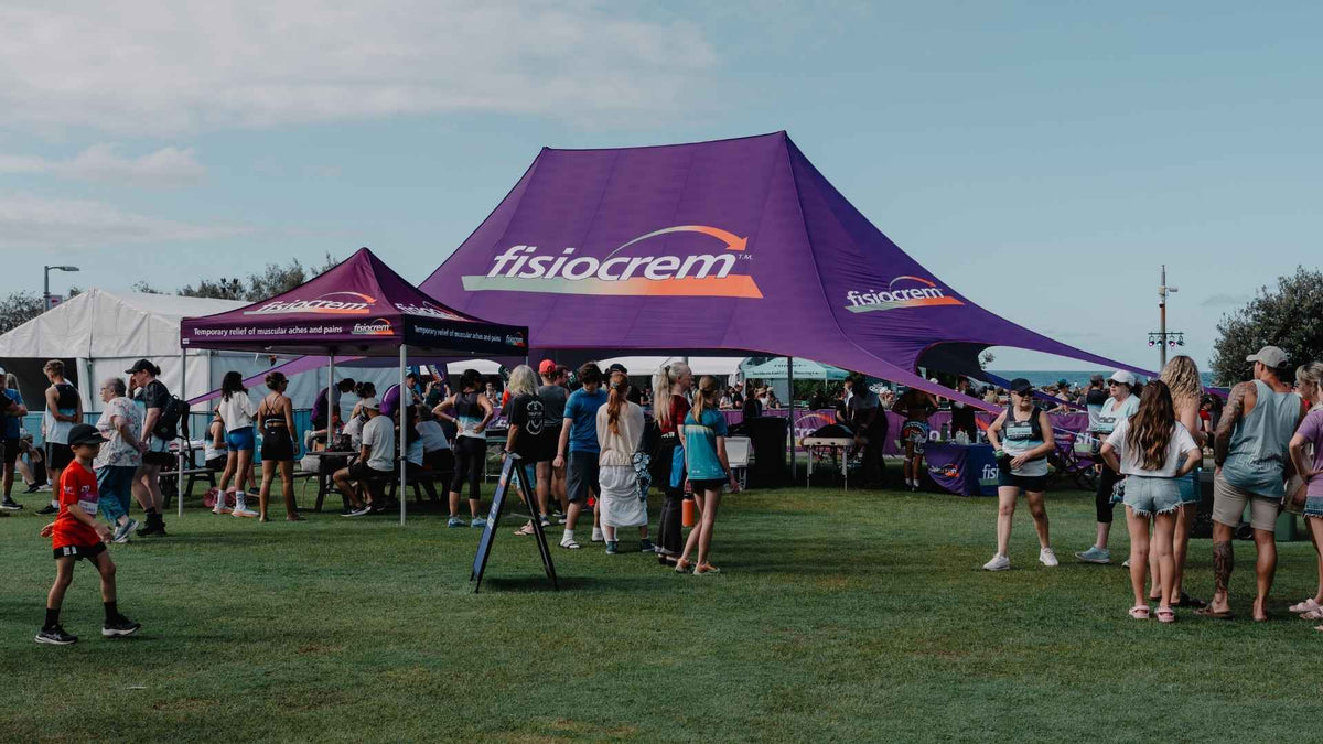 Visitors gathered around a large purple fisiocrem tent at an outdoor event.
