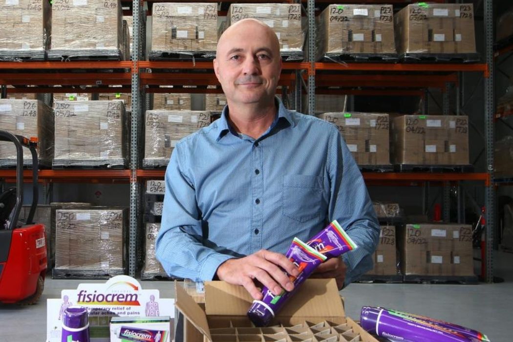 Person holding purple fisiocrem tubes above an open carton in a warehouse.
