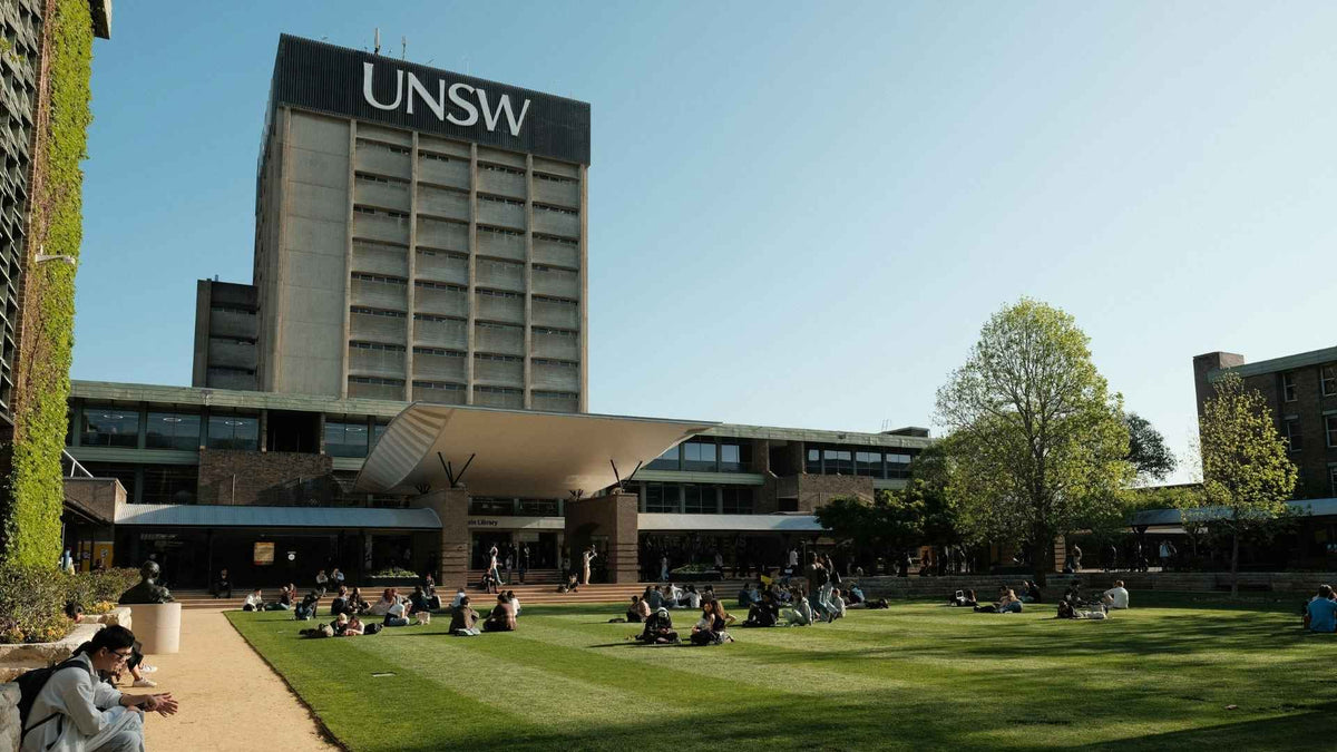 People sitting on a university lawn below a tall building bearing the UNSW sign.