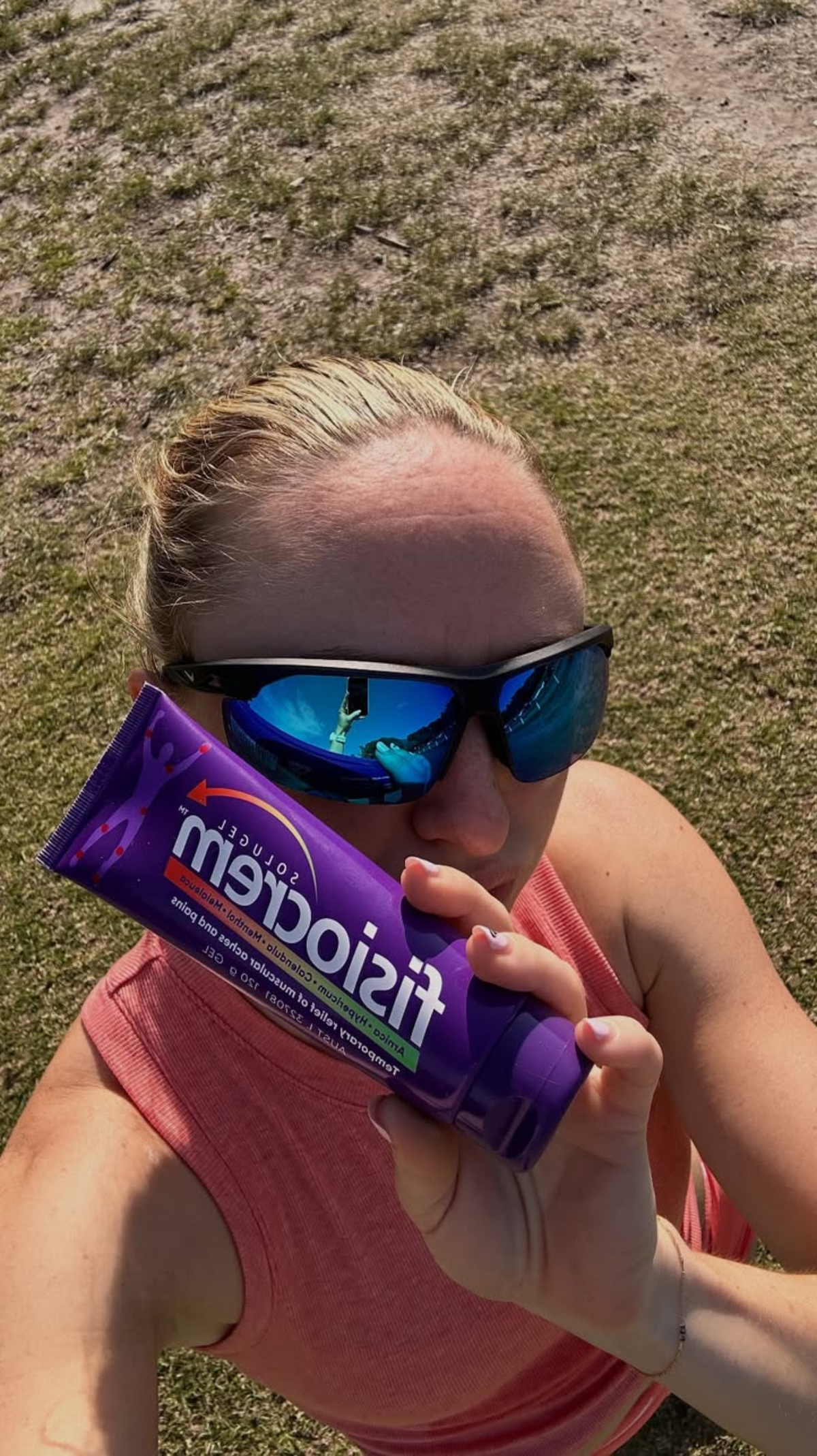 Person in blue mirrored sunglasses taking a selfie while holding a fisiocrem Solugel muscle pain relief cream tube.