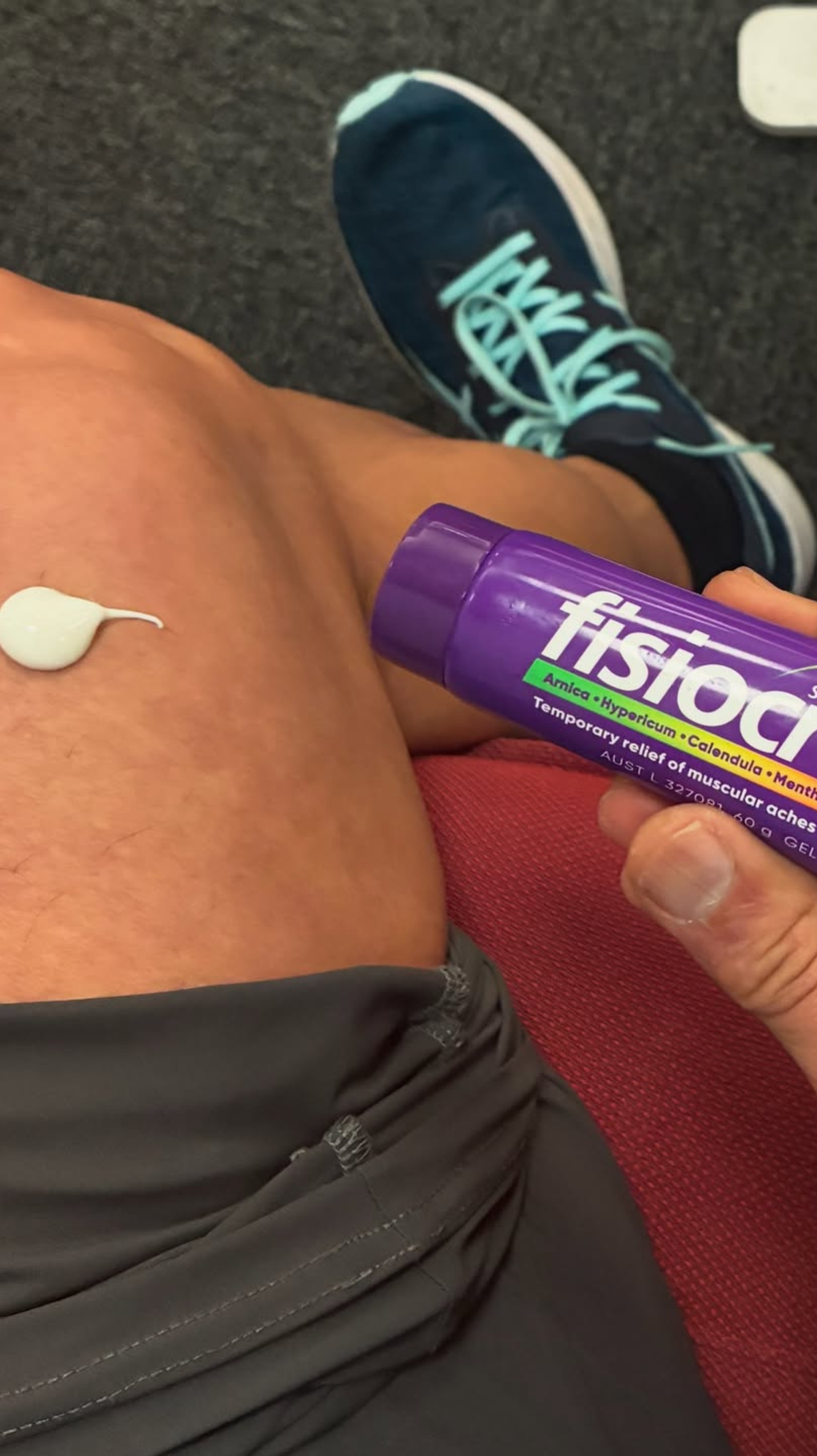 Person holding a fisiocrem Solugel muscle pain relief cream tube beside a dab of white cream on their thigh.