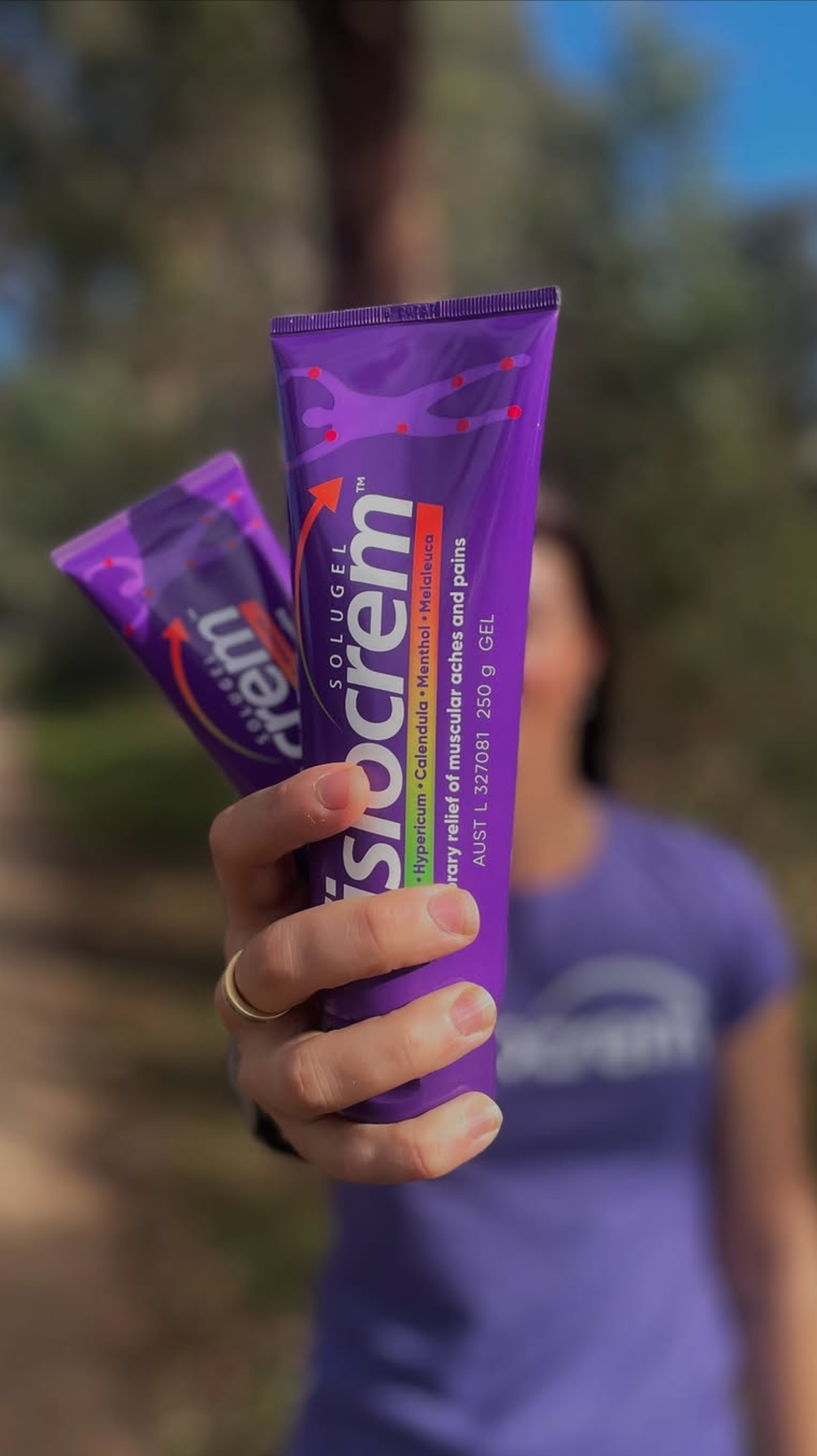 Person holding two fisiocrem Solugel muscle pain relief cream tubes towards the camera outdoors.