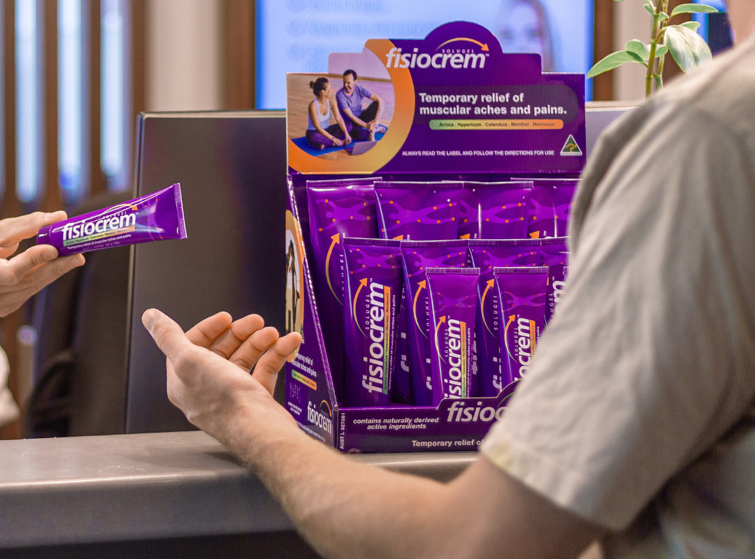 Close-up of a customer receiving a fisiocrem Solugel tube beside a stocked countertop display.