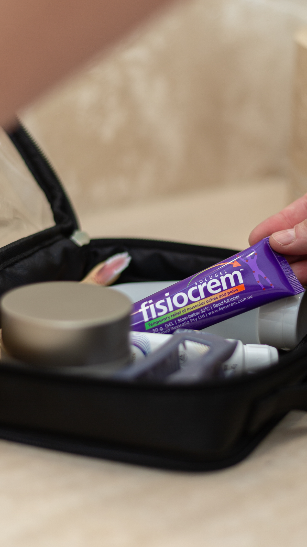 Person placing a fisiocrem Solugel muscle pain relief cream 30g tube inside an open toiletries bag.