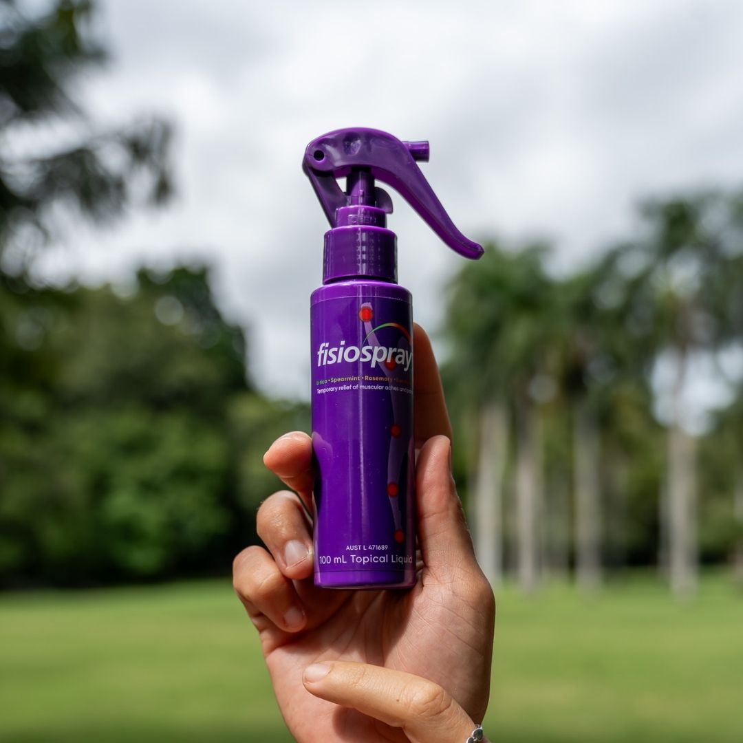 Hand holding a purple fisiospray nerve pain relief spray 100mL bottle outdoors.